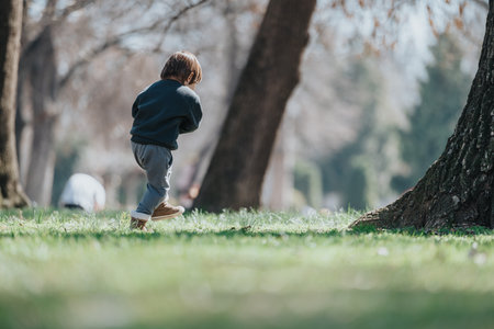 Young child walking outdoors in a park among trees on a sunny dayの写真素材