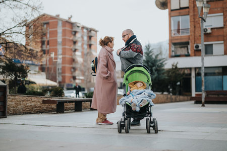 Urban scene of parents talking while their child rests in a stroller with apartments in the backgroundの写真素材