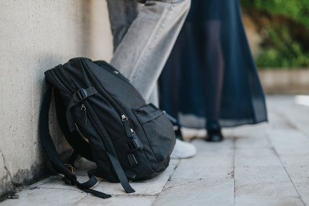 Black backpack resting outdoors near people on a sunny day
