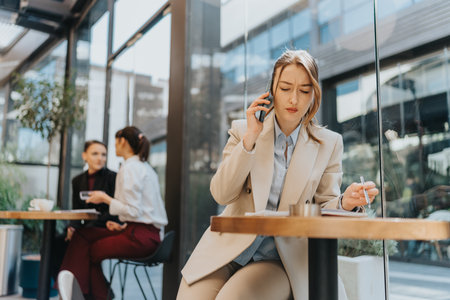 Young entrepreneur talking on a phone and writing notes at an outdoor cafeの写真素材