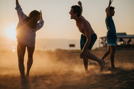 Friends enjoying a playful moment on a sandy beach during sunsetの写真素材