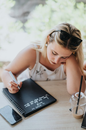 Young woman writing notes in a journal at a casual settingの写真素材