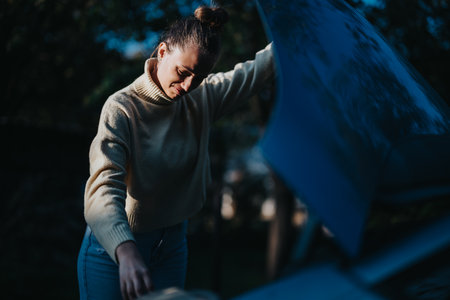 Woman checking a car engine outdoors in a casual sweater and jeansの写真素材