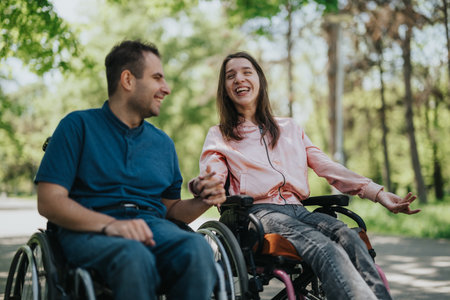 Smiling couple enjoying time outdoors in wheelchairs during a sunny dayの写真素材