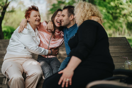 A joyful family gathering with people enjoying laughter on a bench in a sunny park, exemplifying warmth, happiness, and connection.の写真素材
