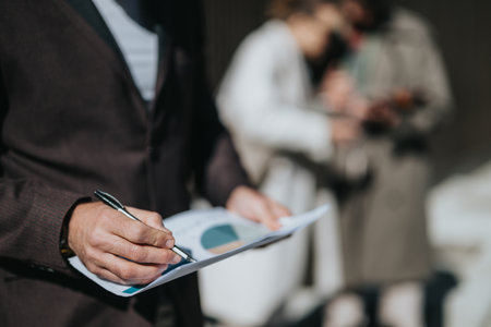 Close-up of a professional reviewing a chart with colleagues in the background outside.の写真素材
