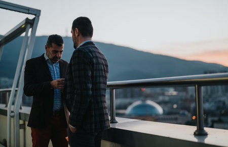 Two business professionals conversing on a rooftop terrace during sunsetの写真素材