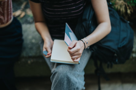 Close-up of a person holding a notebook while sitting outdoorsの写真素材