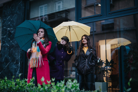 Three women walking on a rainy day while holding colorful umbrellas on a city streetの写真素材