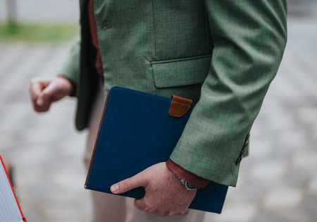 Close-up of an individual holding a notebook outdoors, wearing a green blazerの写真素材