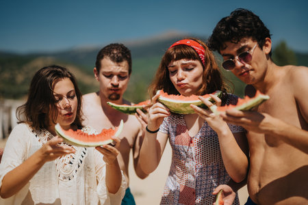 Group of friends enjoying watermelon outdoors during a sunny summer dayの写真素材