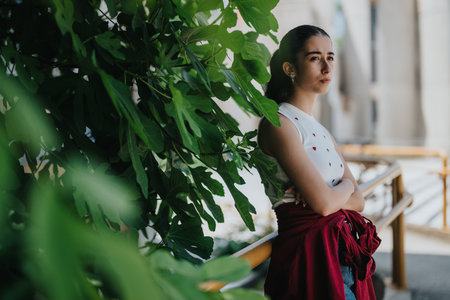 Young woman standing near green plants in an outdoor settingの写真素材