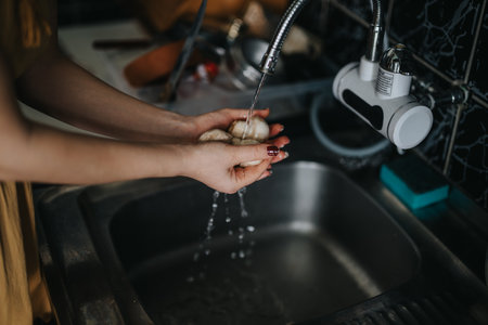 Washing fresh produce under running tap water in a modern kitchen sinkの写真素材
