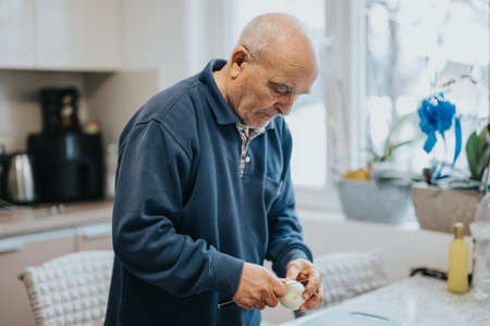 Elderly man peeling vegetables in a modern home kitchenの写真素材