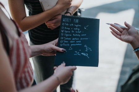Collaborative outdoor group reviewing their weekly planning on a black notepad