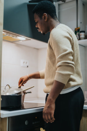 Man preparing food in a modern kitchen, focusing on a stove top pot