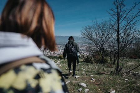 Two people hiking along a trail with a city view in the background under a clear blue sky