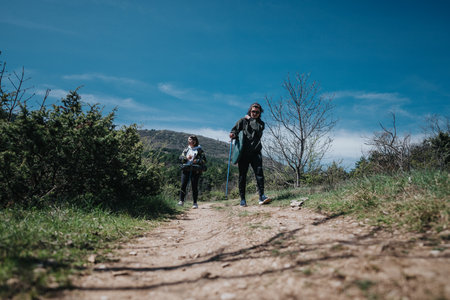 Two individuals hiking on a scenic trail under a bright blue sky