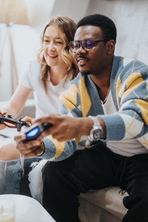 Diverse couple enjoying gaming together at home on a cozy couchの写真素材