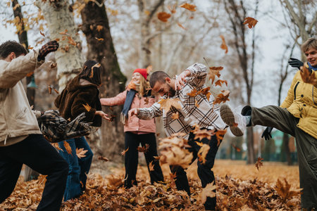 Group of friends enjoying a lively autumn day by playing with fallen leaves in a parkの写真素材