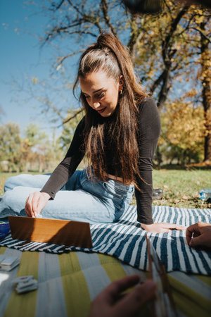 Young woman enjoying a relaxing day outdoors playing a game on a picnic blanket in a sunny park setting with autumn treesの写真素材