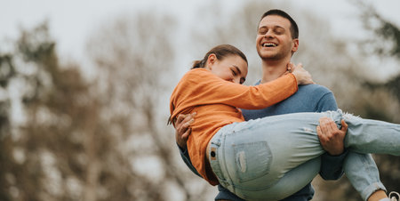Young couple sharing a joyful moment outdoors, man carrying woman playfullyの写真素材