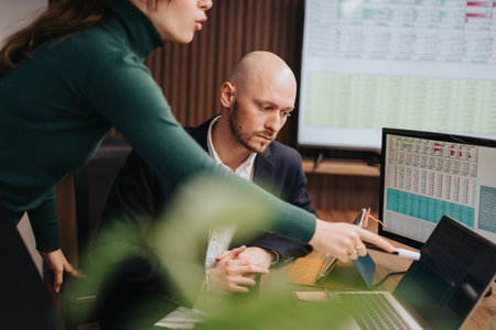 Colleagues discussing data analysis on computer screens in modern office