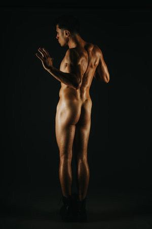 Muscular man posing in dramatic lighting with defined back muscles in focusの写真素材