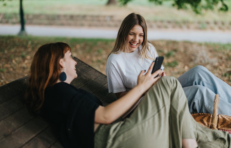 Friends laughing together while relaxing at the park on a sunny dayの写真素材