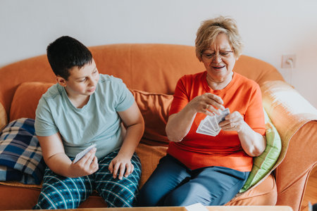 Elderly woman and smiling child playing cards on an orange sofaの写真素材