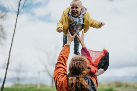 Mother lifting child in the air with joyful expressions outdoorsの写真素材