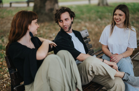 Group of three young adults sitting and talking on a park benchの写真素材