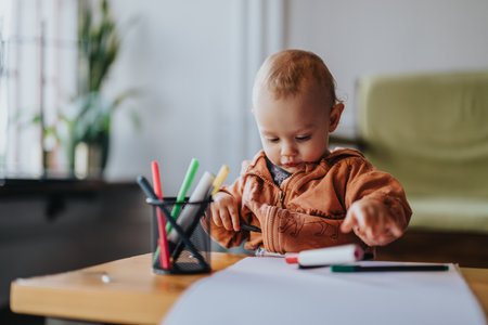 Toddler drawing with colorful markers at a desk in a cozy roomの写真素材