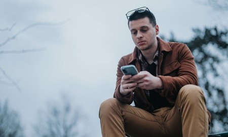 Young man outdoors using smartphone on a cloudy day in the park.の写真素材
