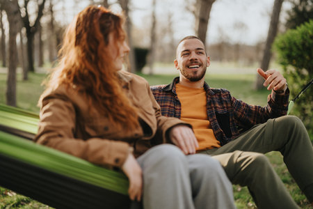 Couple enjoying conversation outdoors while relaxing in a hammock in a parkの写真素材