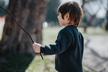 Young child playing outdoors with a stick in a sunny park during springの写真素材