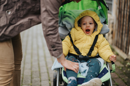 Child in a stroller wearing a yellow jacket on a chilly outdoor dayの写真素材