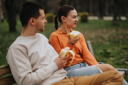 Smiling couple enjoying fruit together on a park bench outdoorsの写真素材