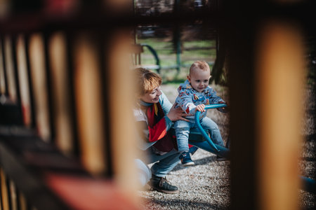 Mother assisting her young child on a playground seesaw outdoorsの写真素材