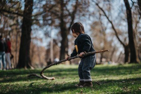 A child playing with a long stick in a sunlit park during autumn among trees