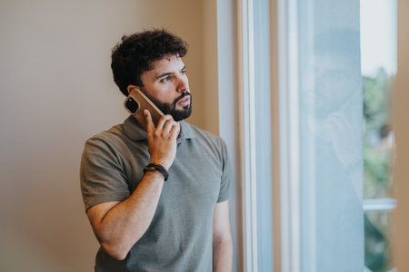 Young man speaking on phone indoors, concerned about financial matters