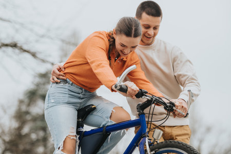 Young couple learning to ride a bicycle outdoors in a park