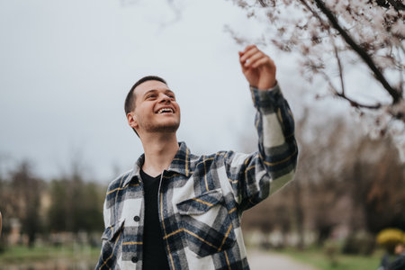 Man Smiling and Reaching For Blossoms in a Scenic Park