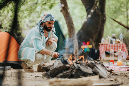 Man Cooking Over Campfire in Forested Campsite With Tent and Supplies