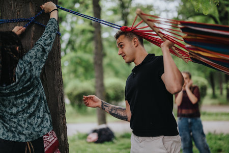 Friends setting up a colorful hammock in a park on a sunny day