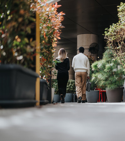 Two people walking outdoors surrounded by large potted plants