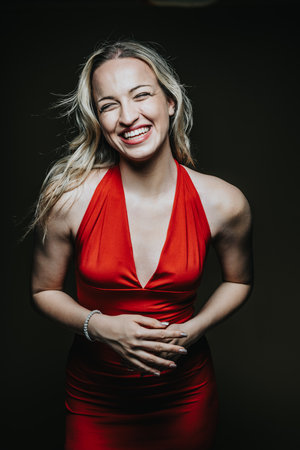 Smiling woman beautifully posing in vibrant red dress under dramatic lightingの写真素材