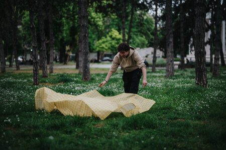 Young person spreading a picnic blanket in a forested park area