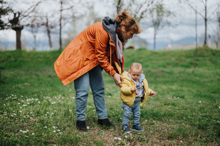 Mother guiding her young child outdoors in a grassy park environment