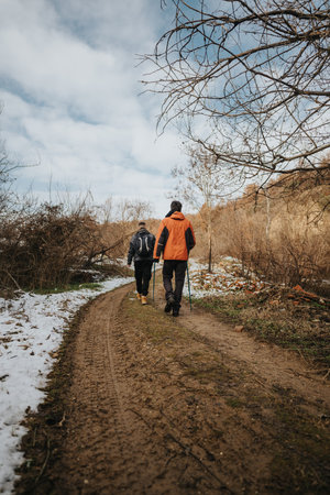 Young people hiking through a scenic winter trail surrounded by bare trees and patches of snow.